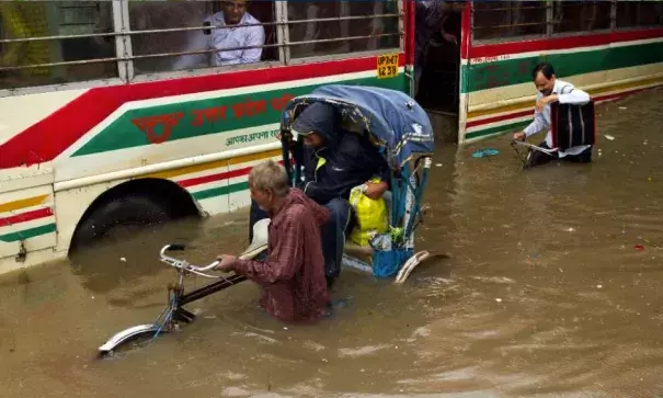 A man from a stranded passenger bus watches an Indian rickshaw puller negotiating through a waterlogged street following heavy rains in Allahabad, India, Tuesday, July 25, 2017. The monsoon season in India runs from June to September. Photo: Rajesh Kumar Singh, AP