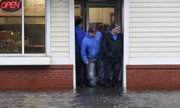 People stand at the entrance to a pizza shop as water floods a street, in Scituate, Mass., March 2, 2018. Photo: Steven Senne, AP