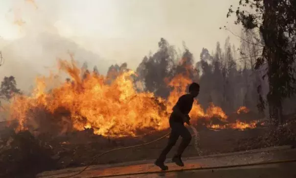 A man runs with a water hose as villagers join firefighters battling a forest fire coming close to houses in the village of Chao de Codes, near Macao, central Portugal, Wednesday, Aug. 16 2017. Photo: Armando Franca, AP