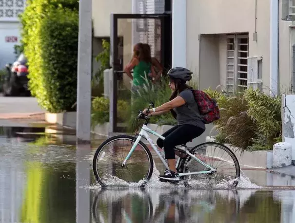 A young student on her bicycle carefully crosses the street on Lincoln Road Court in Miami Beach Thursday where the annual king tide caused flooding. Photo: C.M. Guerrero