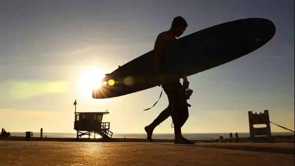 A surfer in Redondo Beach walks past the setting sun on Sunday. Photo: Christina House, Los Angeles Times