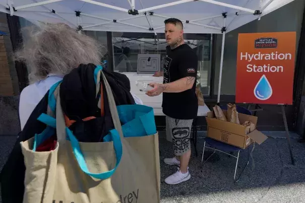 Carlos Ramos hands out bottles of water and sack lunches on Monday at a hydration station in front of the Union Gospel Mission in Seattle. (Ted S. Warren/Associated Press)