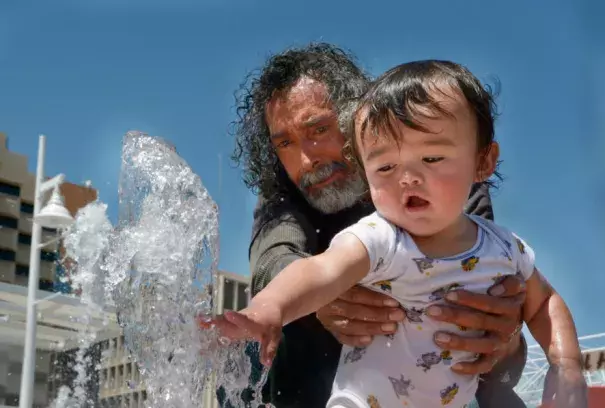 Ernest Espinosa and his grandson, Mariano Espinosa, 1, beat the heat by playing in the Civic Plaza fountain Monday. Albuquerque hit a record high of 98 degrees Monday, but temperatures will drop slightly this week as a cold front pushes into New Mexico. Credit: Greg Sorber, Albuquerque Journal