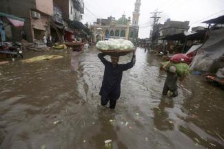 Laborers carry produce as they wade through a flooded road after heavy rainfall, in Lahore, Pakistan, Thursday, July 21, 2022. (Credit: AP Photo/K.M. Chaudary)