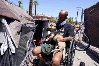 "Cueball" pets his dog Lindsay at their tent on the edge of a homeless encampment Friday, May 20, 2022, in Phoenix. Hundreds of homeless people die in the streets each year from the heat, in cities around the U.S. and the world. The ranks of homeless have swelled after the pandemic and temperatures fueled by climate change soar. (Credit: AP Photo/Ross D. Franklin)