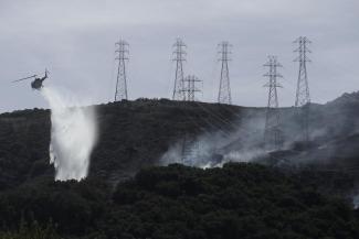 FILE - In this Oct. 10, 2019, file photo, a helicopter drops water near power lines and electrical towers while working at a fire on San Bruno Mountain near Brisbane, Calif. California energy leaders on Friday, May 6, 2022 said the state may see an energy shortfall this summer. Threats from drought, extreme heat and wildfires, are among the issues that will create challenges for energy reliability this summer and in the coming years. (Credit: AP Photo/Jeff Chiu, File)