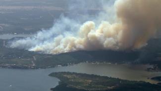 In this image taken from video, smoke from a wildfire rises in Palo Pinto County, Texas on Monday, July 18, 2022. A wildfire has burned at least five homes and resulted in about 300 homes being evacuated around a lake in north Texas amid sweltering temperatures and dry conditions, authorities said. (Credit: KDFW FOX 4 via AP)