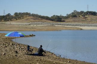 A man places his fishing pole along the shore line of Folsom Lake that would normally be underwater in Folsom, Calif., Monday, Oct. 3, 2022. The reservoir is filled to about 70% of its historical average as California began its new water year that started Oct. 1. The past three years have been California's driest on record and state officials said Monday that they're preparing for the streak to continue. (AP Photo/Rich Pedroncelli)