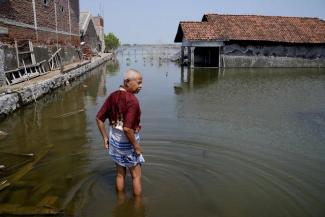 FILE - Sukarman walks on a flooded pathway outside his house in Timbulsloko, Central Java, Indonesia, July 30, 2022. (Credit: AP Photo/Dita Alangkara, File)