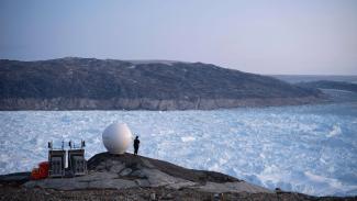 A person stands next to an antenna at the Helheim glacier in Greenland. (Credit: Felipe Dana/AP)