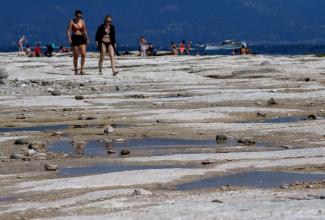 People walk as underwater rocks emerge from the water of Lake Garda after northern Italy experienced the worst drought in 70 years in Sirmione, Italy, August 16, 2022. (Credit: REUTERS/Flavio Lo Scalzo/File Photo)