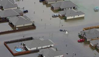 FILE- A boat motors between flooded homes after heavy rains inundating the region, in Hammond, La., on Aug. 13, 2016. A new study Thursday, May 18, 2023, finds the natural burst of El Nino warming that changes weather worldwide is far costlier with longer-lasting expenses than experts had thought, averaging trillions of dollars in damage. (Credit: AP Photo/Max Becherer, File)