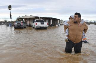 Ryan Orosco, of Brentwood, carries his son Johnny, 7, on his back while his wife Amanda Orosco waits at the front porch to be rescued from their flooded home on Bixler Road in Brentwood, Calif., Jan. 16, 2023. (Credit: Jose Carlos Fajardo/Bay Area News Group via AP, File)
