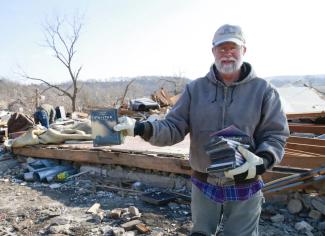A man, Larry Stout, is shown holding up the movie "Twister" amid the remains of his sister's home, which was hit by a tornado.