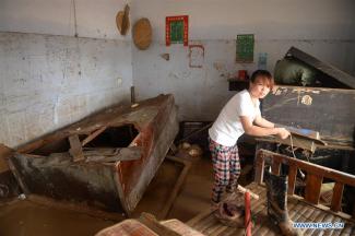 A villager clears the debris at her home in Nanshitun village of Xingtai City, north China's Hebei Province, July 24, 2016. Torrential rain and floods have left 34 people dead and 13 people missing in Xingtai City by Sunday as well as some 9,200 homes were still without electricity. Photo: Xinhua