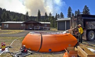 Nathan Smith of Arlee fills a 6,000 gallon portable tank with water at a residence off Quartz Road near Lozeau as smoke from the Sunrise fire rises in the background on Monday. On Wednesday, evacuations were ordered and the fire became the highest priority in the nation. Photo: Tom Bauer, Missoulian
