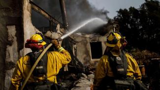 Humboldt County firefighters Bobby Gray, left, hoses down smoldering flames inside a destroyed home Marcus Yam, Los Angeles Times