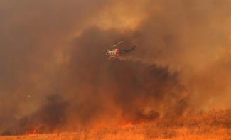A helicopter drops water on a wind driven wildfire in Orange, California, U.S., October 9, 2017. Photo: Mike Blake, Reuters